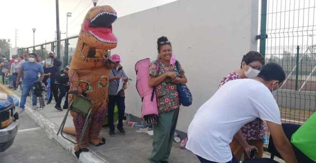 Hombre vestido de dinosaurio acompaña a su madre a vacunarse contra el Covid-19